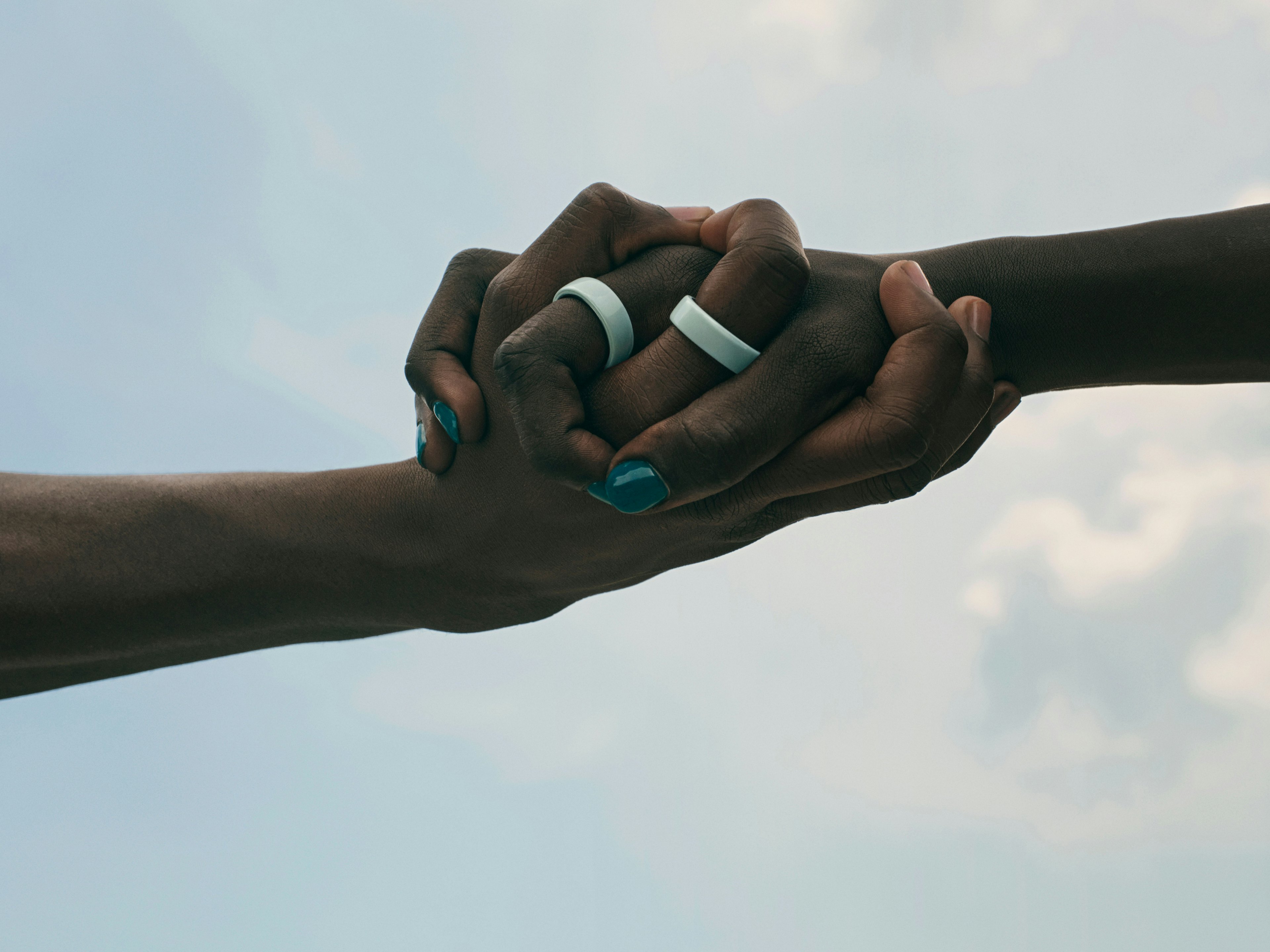 A close-up of two hands holding each other, each wearing an Oura Ring 4 Ceramic on the index finger.