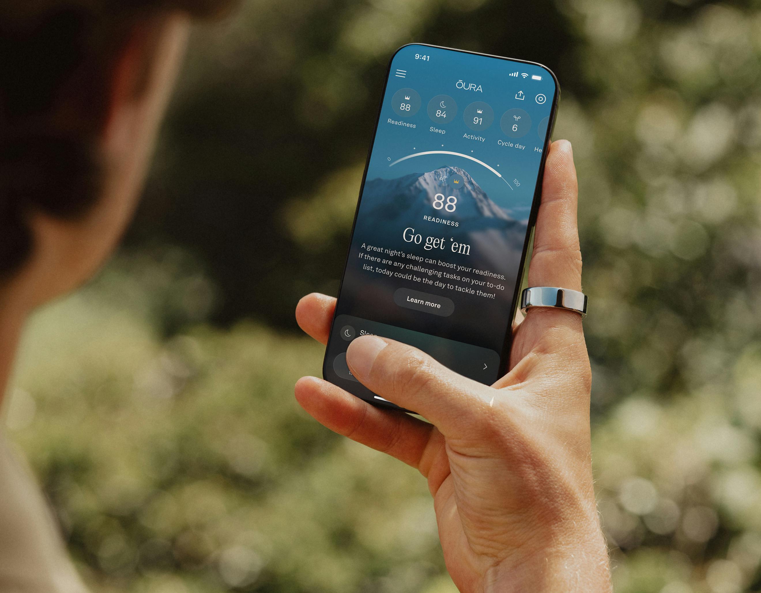 A person views the Oura app on their smartphone while wearing an Oura ring on their right index finger